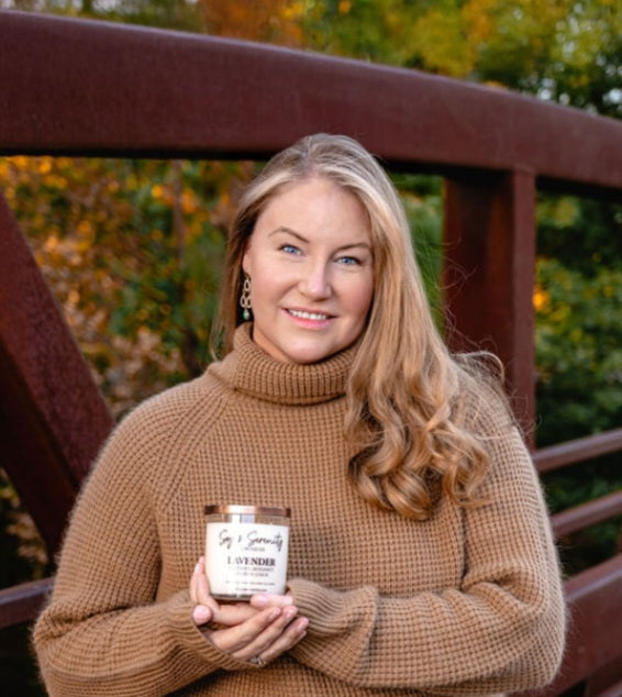 Shelley Richards holding a Soy & Serenity soy candle in a fall setting.